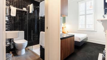 Un baño moderno con ducha revestida de azulejos negros, inodoro blanco y tocador de madera con lavabo.