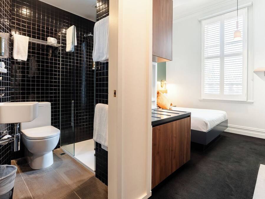 Un baño moderno con ducha revestida de azulejos negros, inodoro blanco y tocador de madera con lavabo.