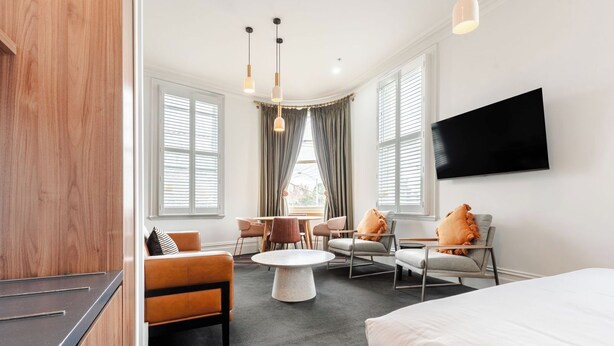 Una habitación de hotel moderna con una cama, una mesa de comedor con sillas, un sofá y un televisor colgado en la pared.