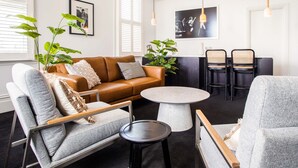 Una sala moderna con un sofá de cuero marrón, sillones grises, una mesa de centro redonda y un comedor con sillas y mesa negros.
