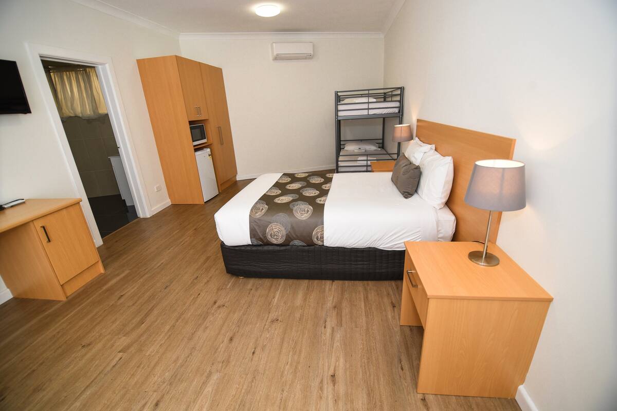 Ein Schlafzimmer mit Etagenbett, Nachttisch, Lampe, Kleiderschrank und einem Fernseher an der Wand.