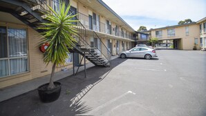 Un motel a più piani con un parcheggio, una scala che conduce ai piani superiori e una palma sullo sfondo.