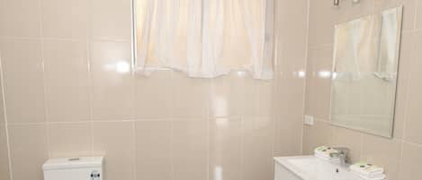 Baño con inodoro, lavabo, espejo y ventana con cortinas.