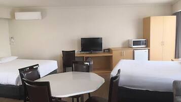 Une chambre d’hôtel avec deux lits, un bureau avec une télévision, un four à micro-ondes et un petit réfrigérateur.