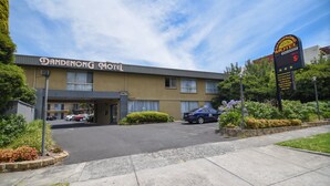Un motel a Dandenong con un parcheggio, una targa e un cielo sereno.