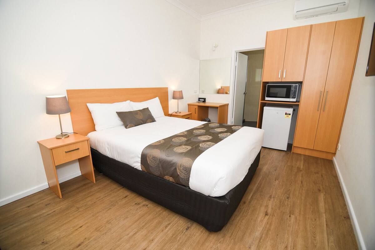 Ein Hotelzimmer mit Bett, Nachttischen, einer Mikrowelle, einem Kühlschrank und einem Kleiderschrank.