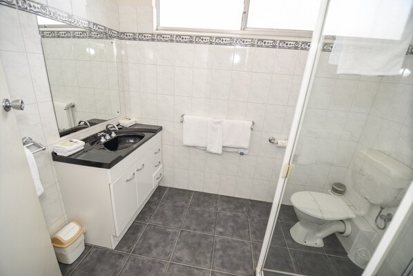 A bathroom with a sink, mirror, white tiles, a toilet, and a shower area.