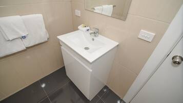 Un baño con lavamanos blanco, espejo y toallero.