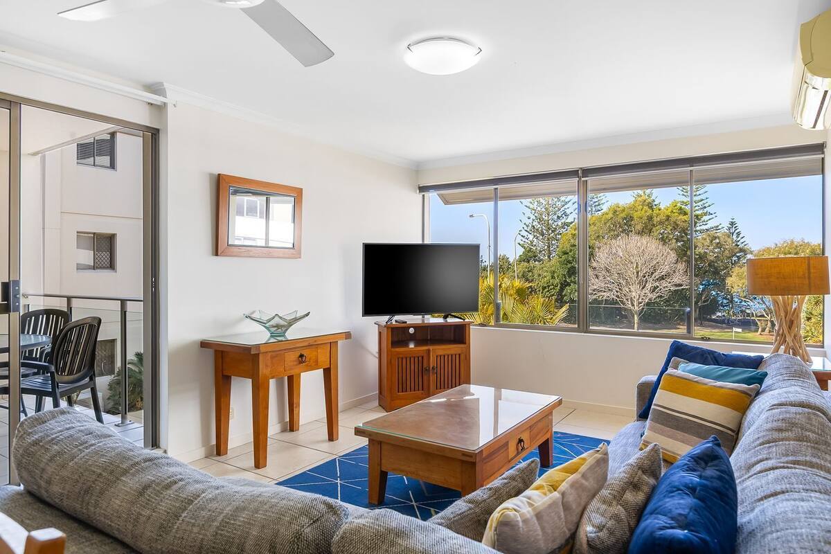 A modern living room with a sofa, coffee table, TV, and a balcony with chairs.