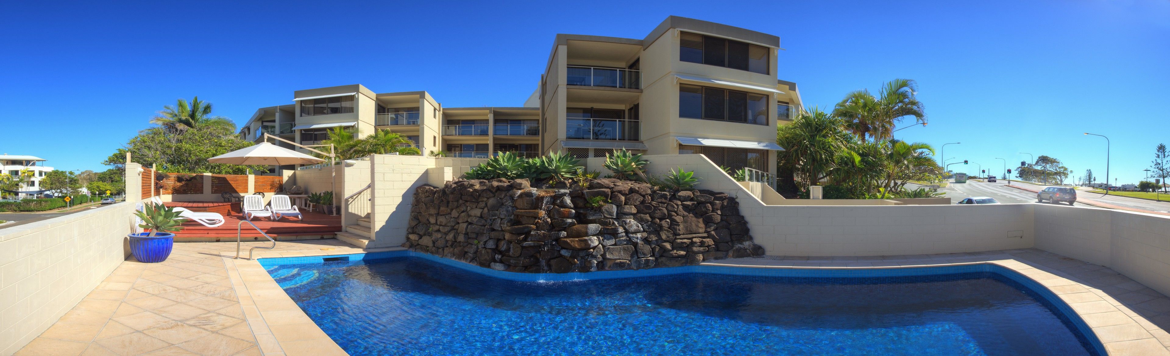 Un hotel moderno con piscina, pared de piedra y varios balcones.