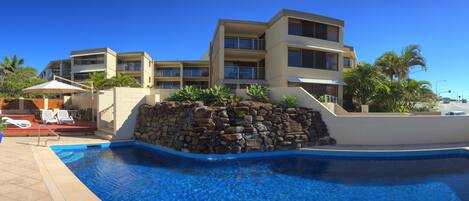 Un hotel moderno con piscina, pared de piedra y varios balcones.