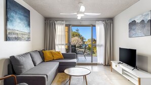 Ein modernes Wohnzimmer mit grauem Sofa, rundem Couchtisch, flachbildfernseher auf weißem Standfuß und Deckenventilator.