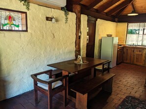 Enjoy cooking in this kitchen with a wooden table and benches, a refrigerator, and a window with a decorative flower.