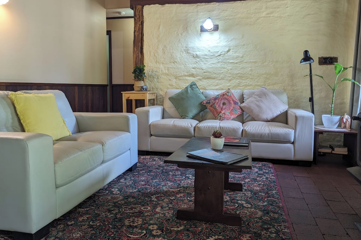 A living room with two white sofas, a patterned rug, a small wooden coffee table, and a wall-mounted light fixture.