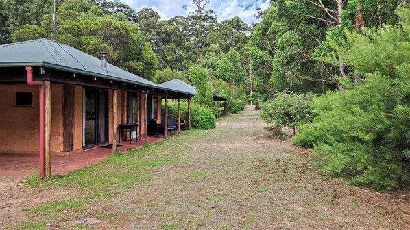 Relax on the covered porch with a table and chairs, surrounded by lush greenery and trees.