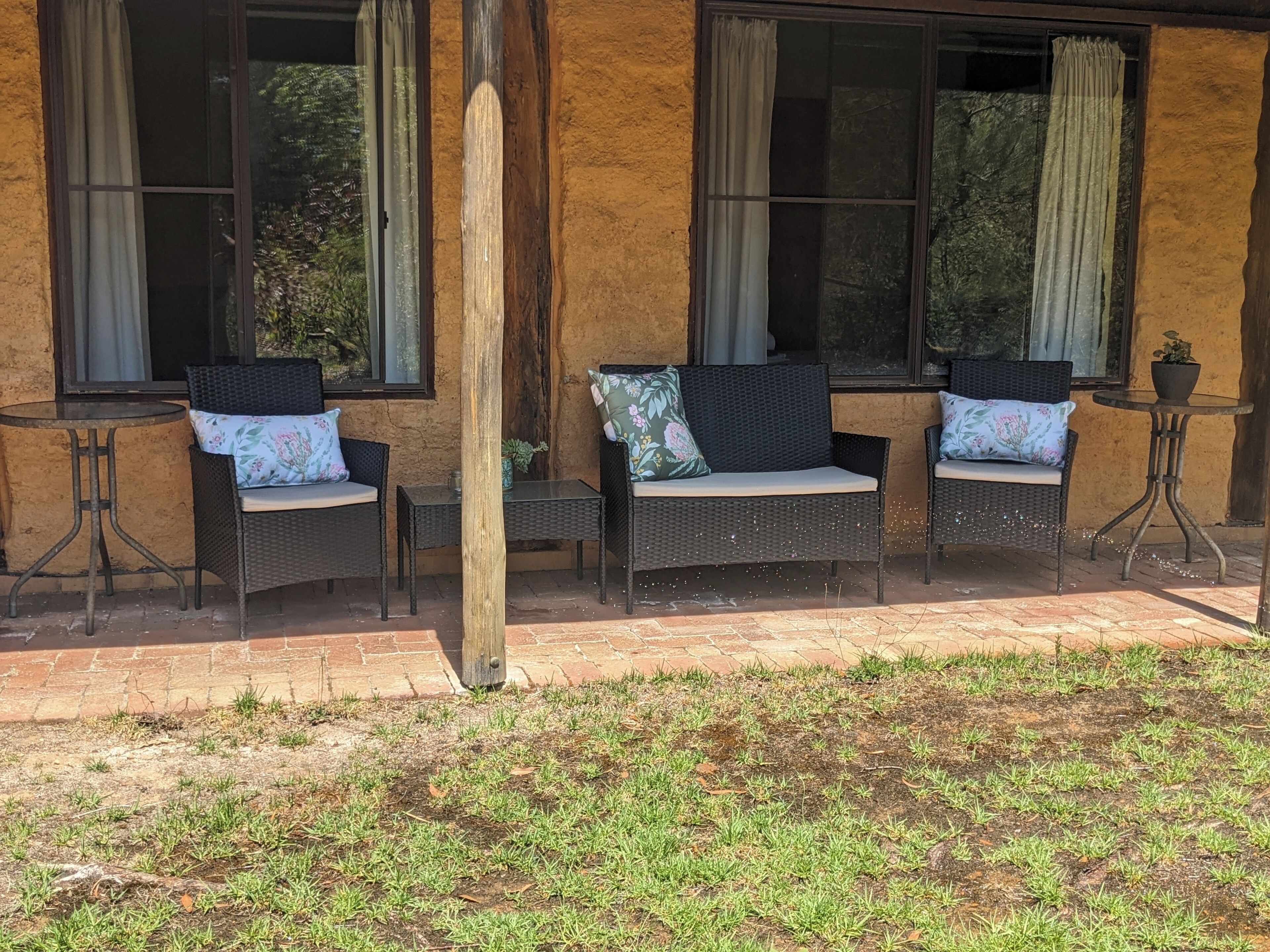 An outdoor seating area with wicker furniture and cushions, a small table, and a potted plant.
