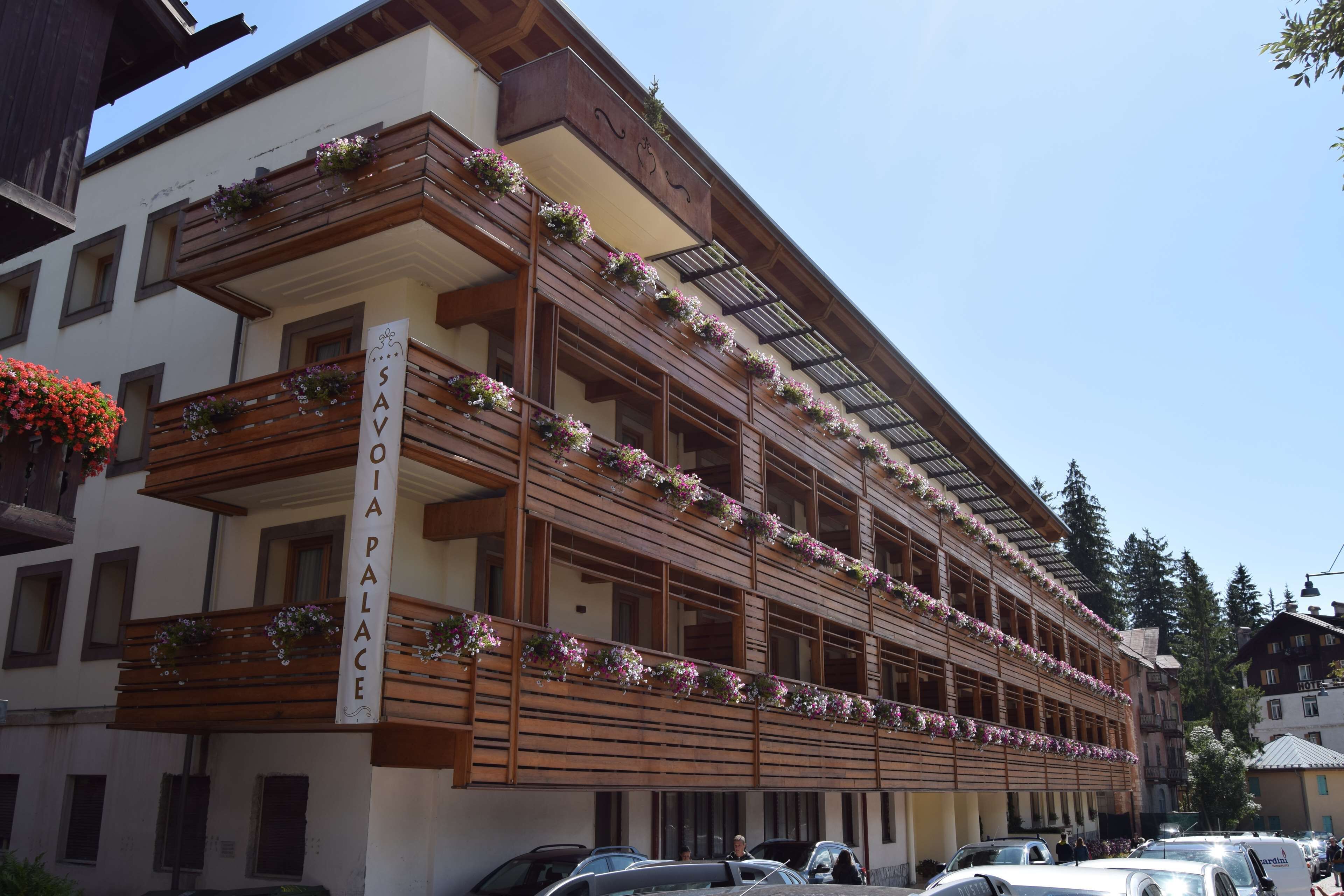 Un hotel de varios pisos con balcones decorados con flores, un cartel que dice "SAVIA PALACE" y un estilo arquitectónico clásico.