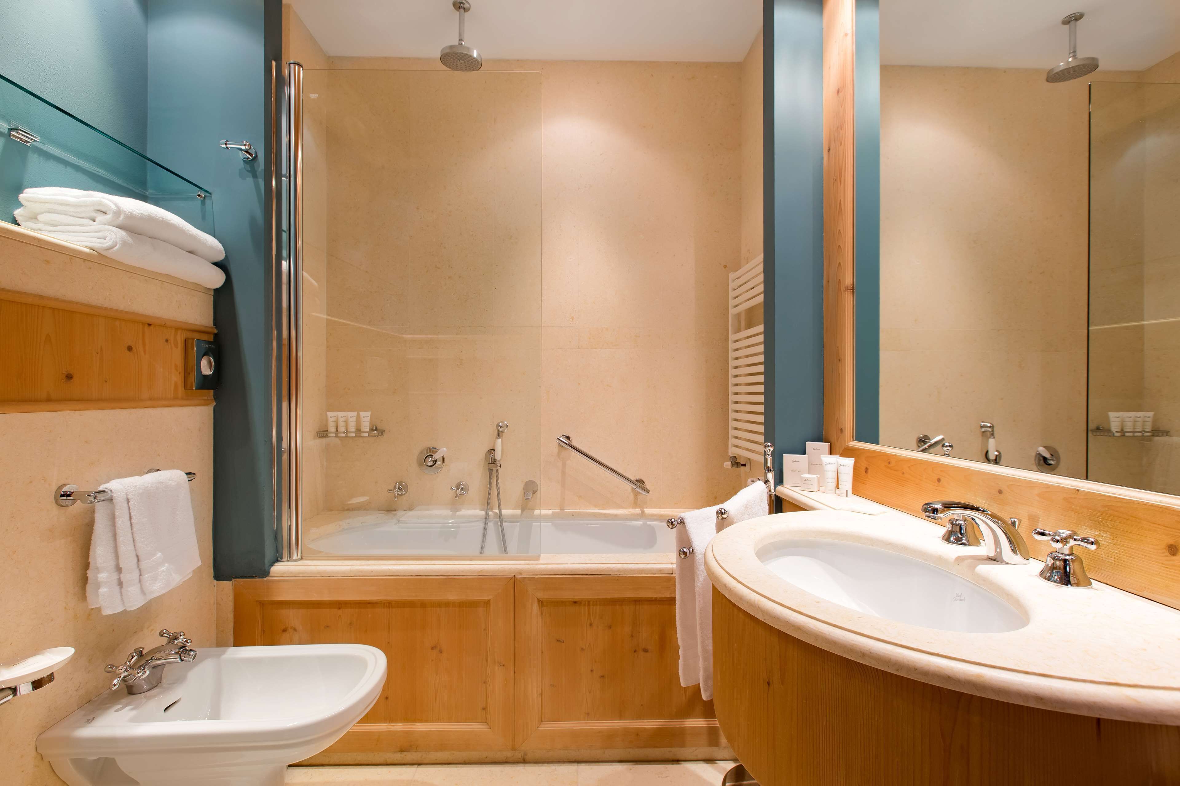 Een moderne badkamer met een houten wastafelmeubel, een vrijstaand bad, een grote spiegel en een wastafel.