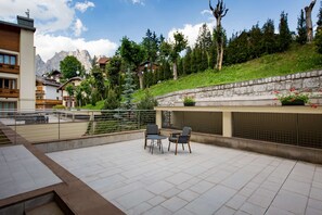 Una terraza con pared de piedra, una mesa con sillas y vista a un paisaje montañoso.