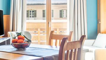 Ein Holzespeisetisch mit Stühlen, eine Obstschale und Blick auf ein Gebäude durch ein Fenster.
