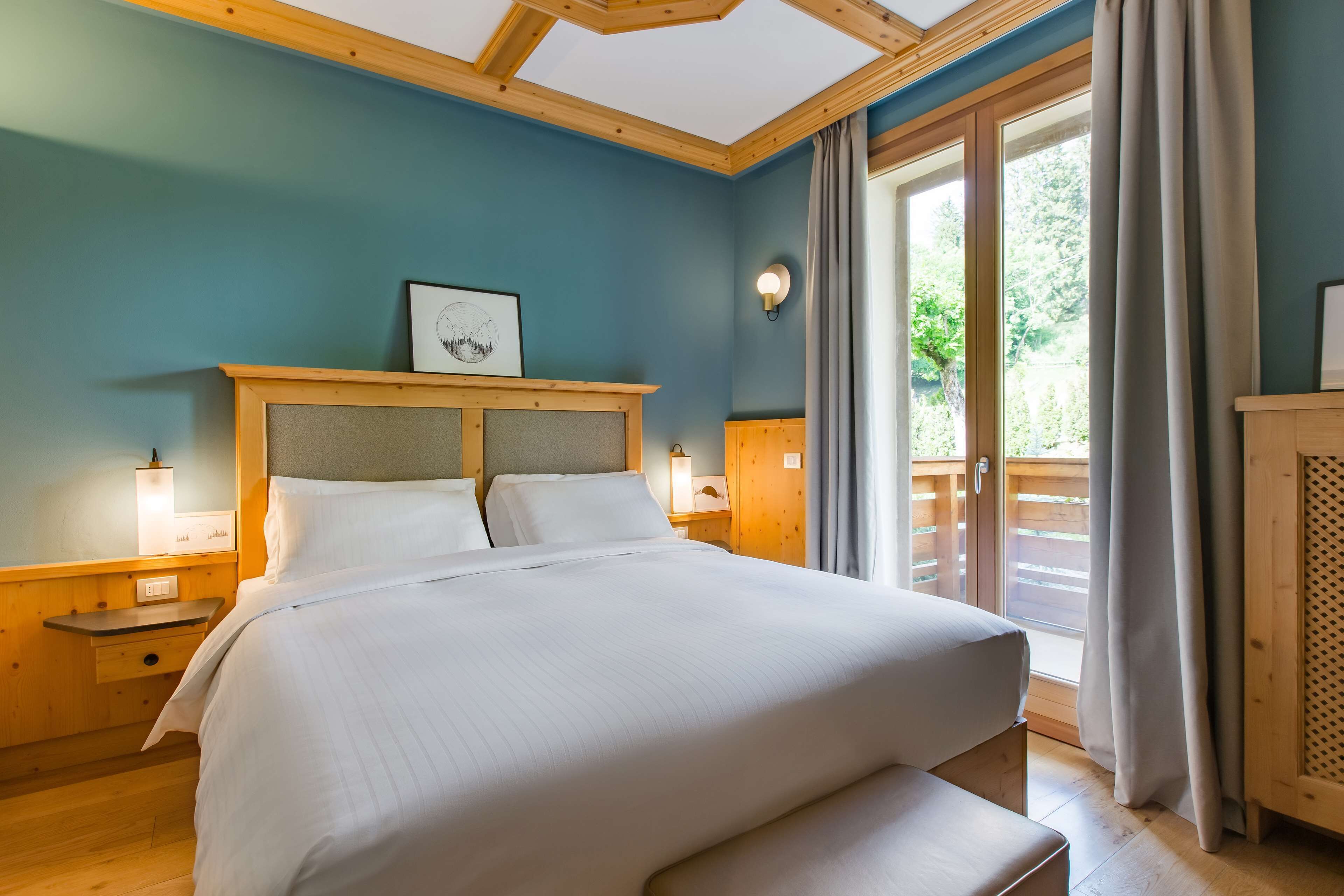 A bedroom with a large bed, wooden headboard, bedside tables with lamps, and a view of the outdoors through a sliding door.