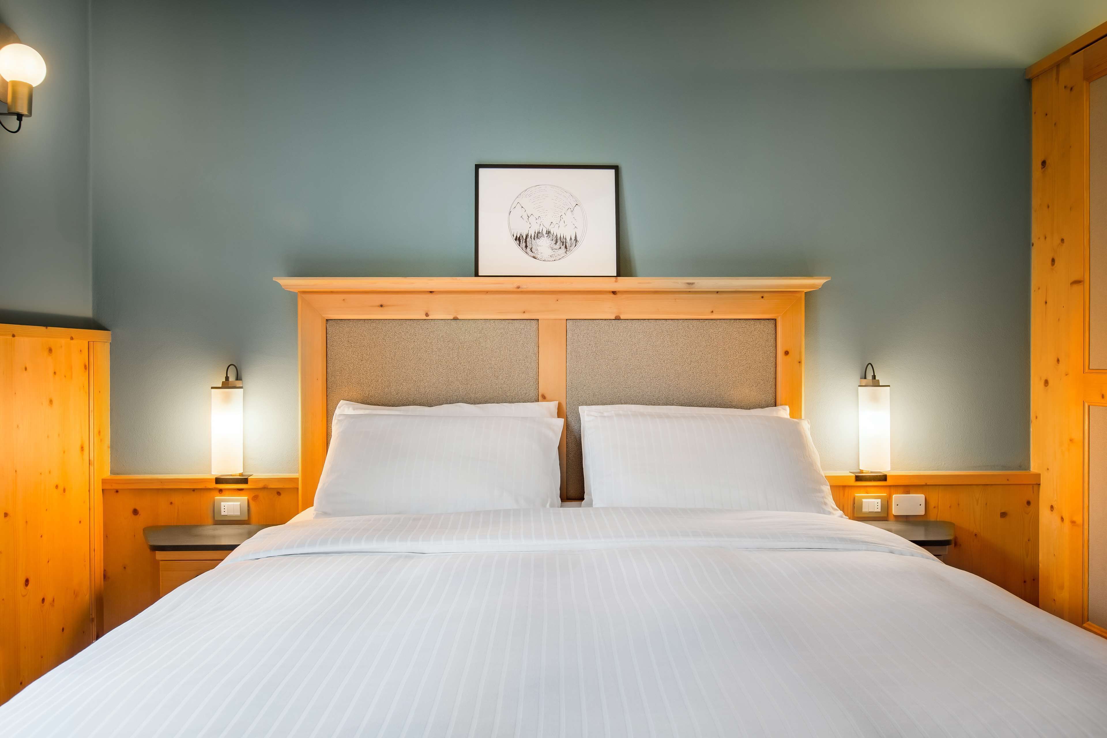 Una cama bien hecha con sábanas blancas, un cabecero de madera y dos lámparas de noche.