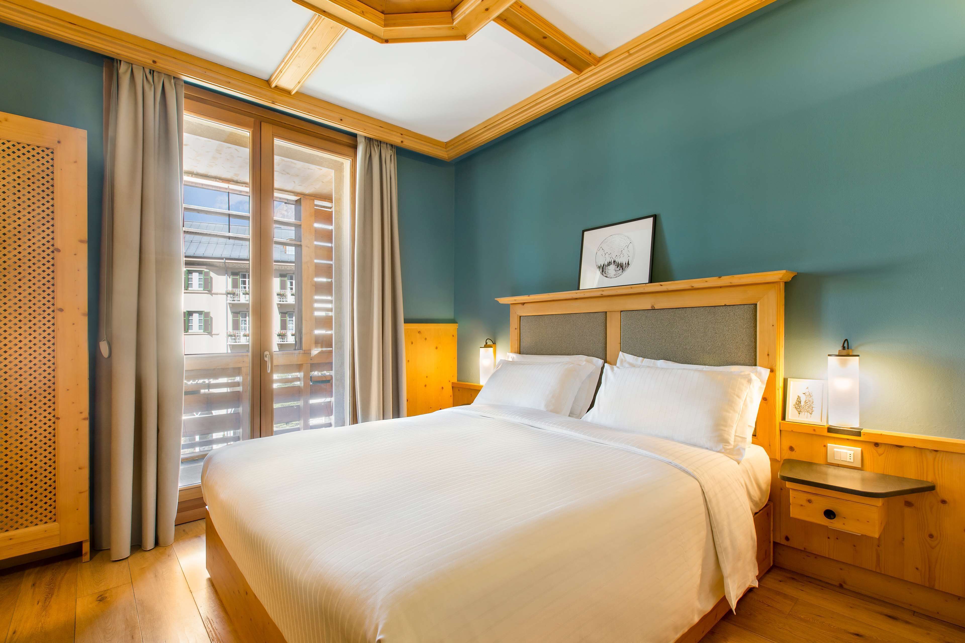 A hotel room with a large bed, wooden headboard, and a view of buildings through the window.