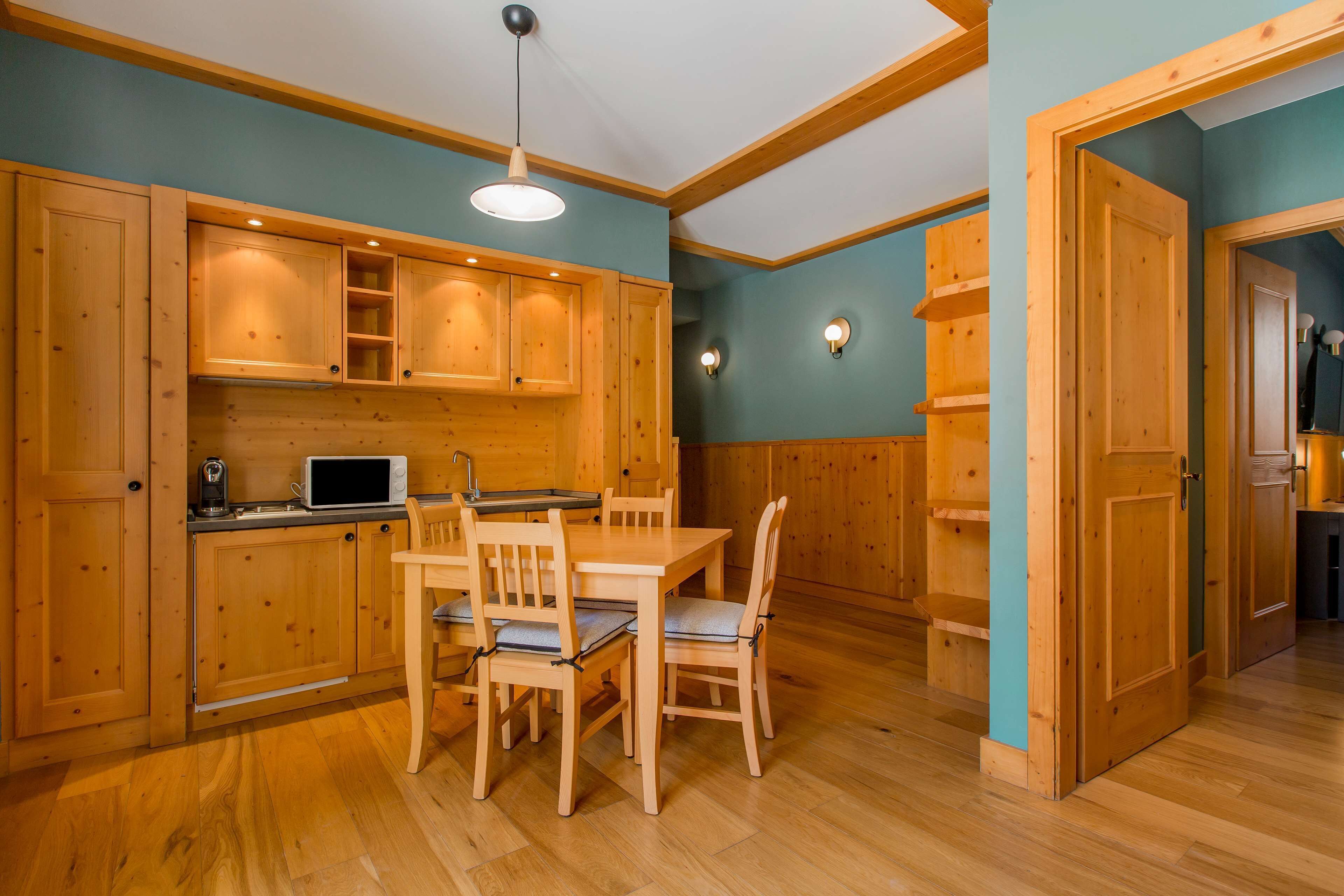 A wooden kitchen with a dining table and chairs, wooden cabinets, and a microwave.