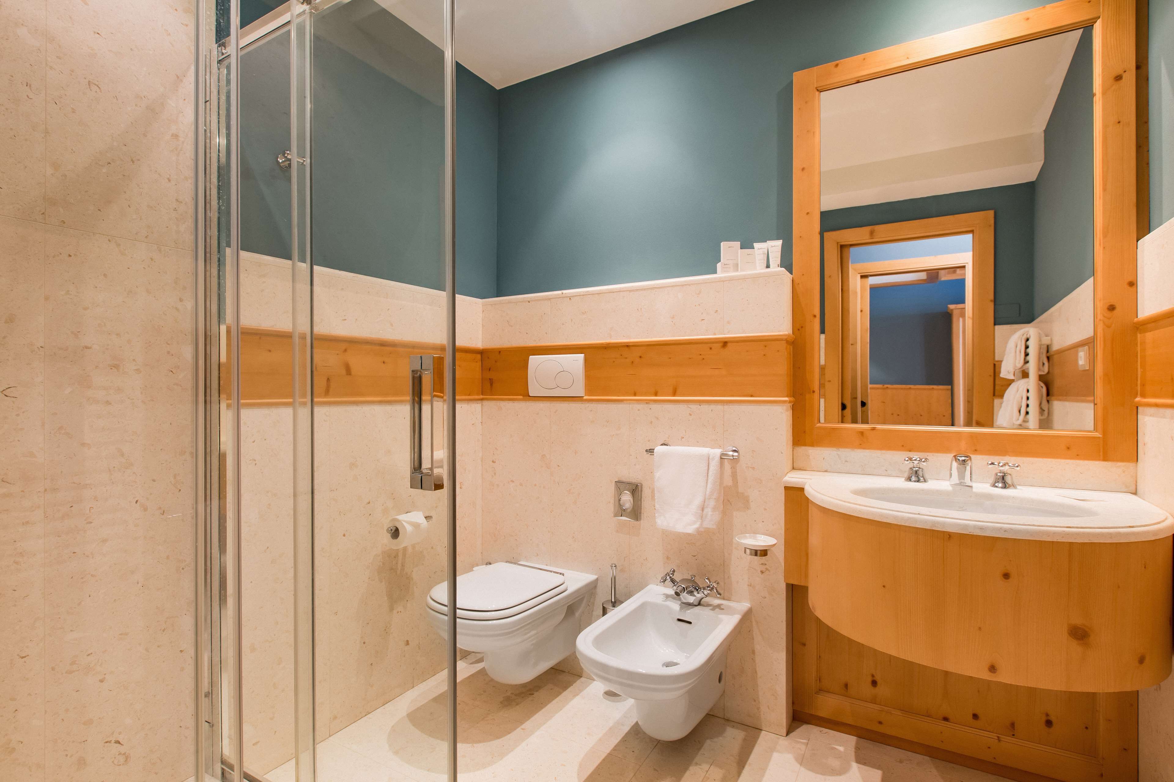 Un baño moderno con cabina de ducha de vidrio, inodoro, bidé y tocador de madera con lavamanos.