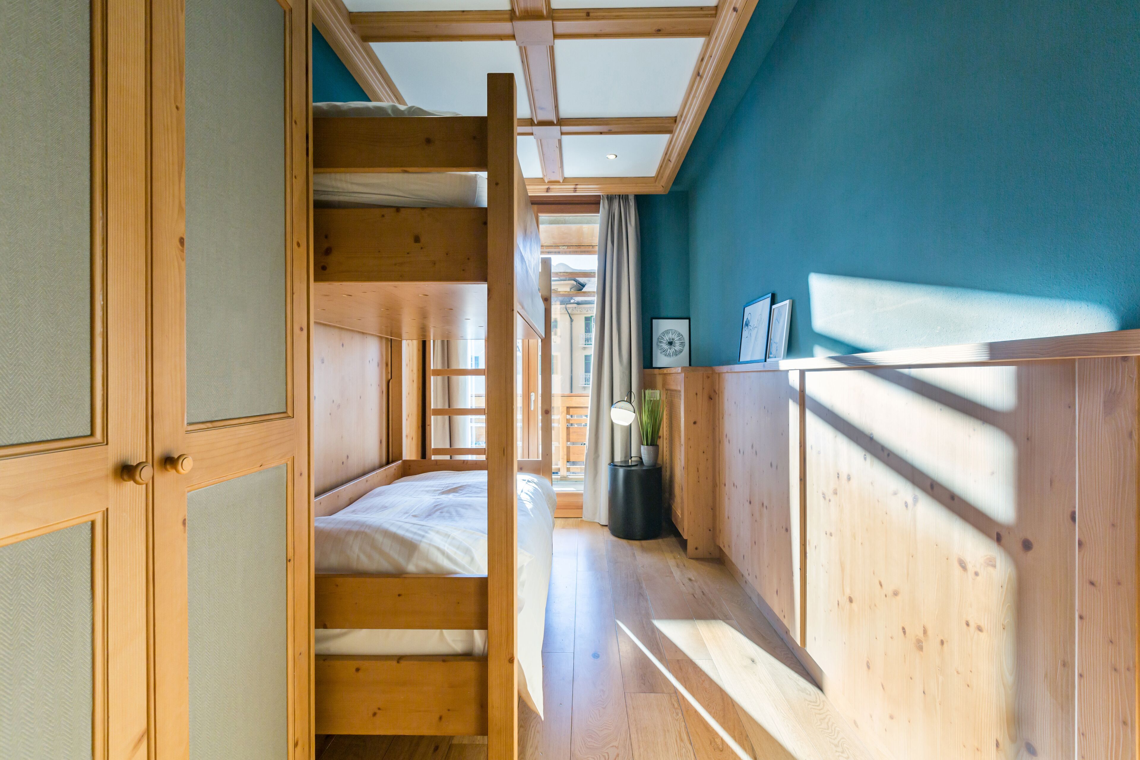 A wooden interior with a bunk bed, a desk, and a window.