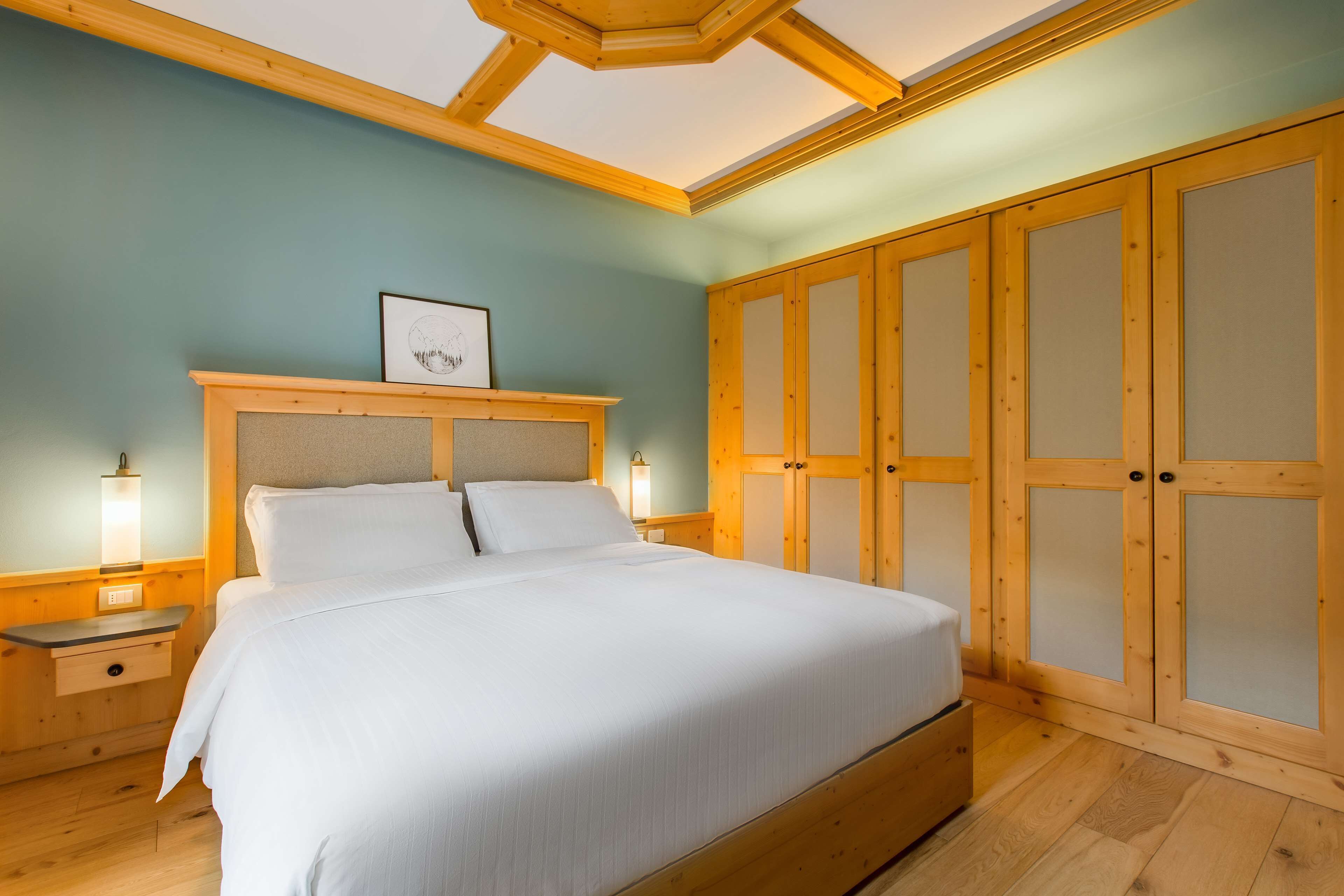 A bedroom with a large bed, wooden wardrobe, and bedside tables with lamps.