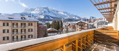A balcony with a wooden railing overlooking a snowy mountain and buildings.
