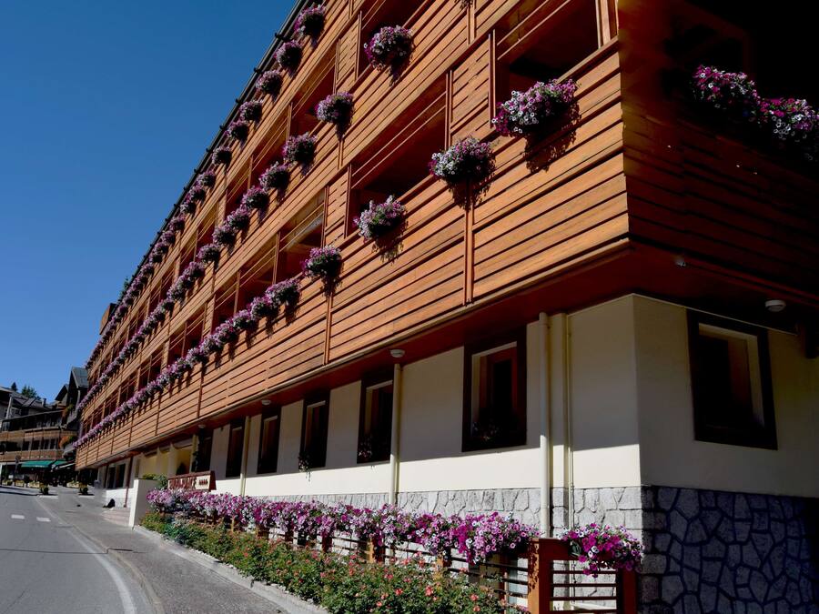 A hotel with a wooden facade, multiple balconies with flower boxes, and a stone wall at the base.