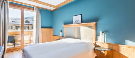A bedroom with a large bed, wooden headboard, a bedside table, and a view of a balcony.