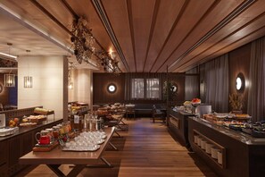 Amplia zona de buffet con mesas de madera y una gran variedad de alimentos y bebidas.