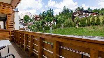 A wooden balcony with a table and chairs, overlooking a hillside with houses and trees.
