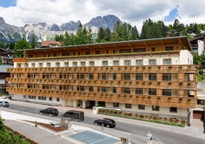 Un hotel de varios pisos con un diseño moderno, con balcones con plantas, un letrero que indica 'Spree Palace Residences' y vistas de montañas al fondo.