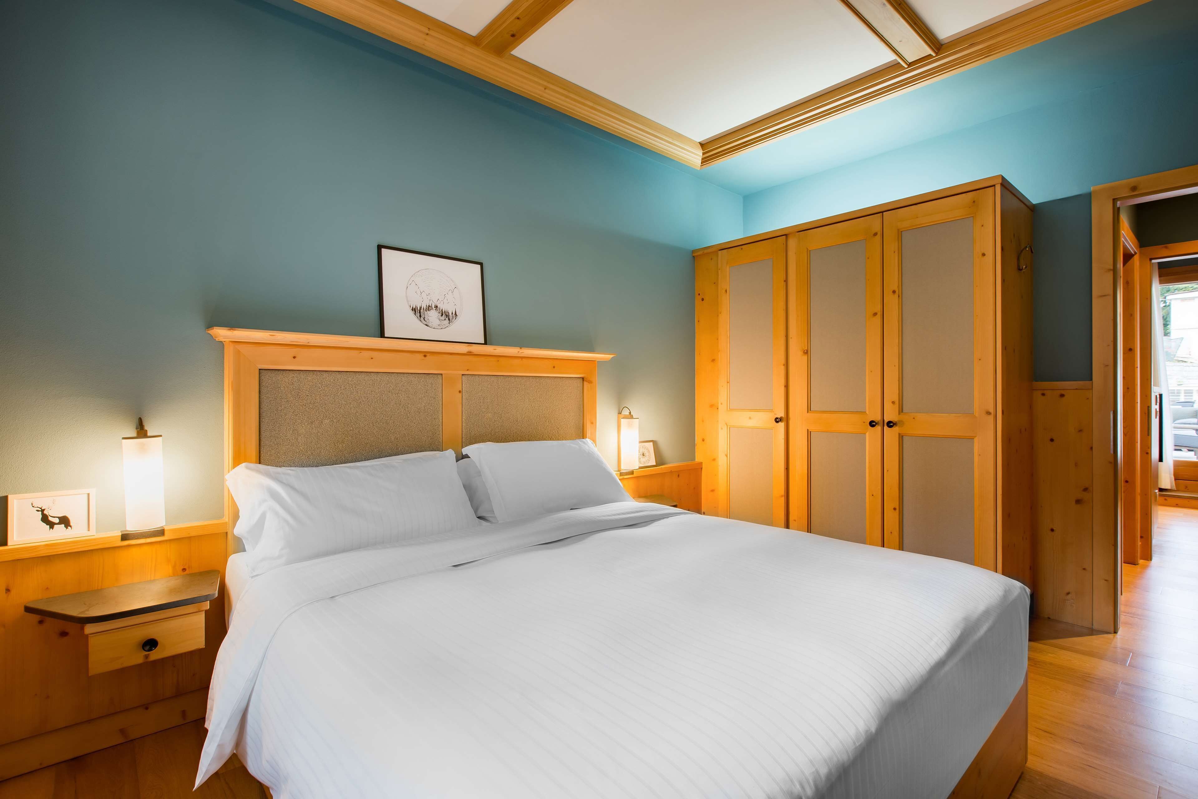 A bedroom with a bed, wooden wardrobe, nightstands, and a framed picture on the wall.