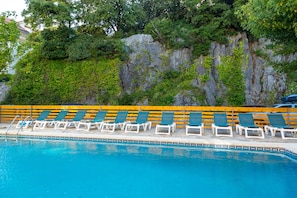 Relax by the pool surrounded by lush greenery and a natural rock formation.