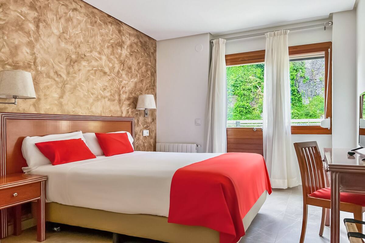 Ein Hotelzimmer mit Bett, Schreibtisch und einem fenster mit Vorhängen.