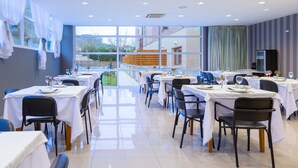 A modern dining area with tables set for meals, large windows, and a view of the outdoors. - Hotel Los Arces (Arnuero)