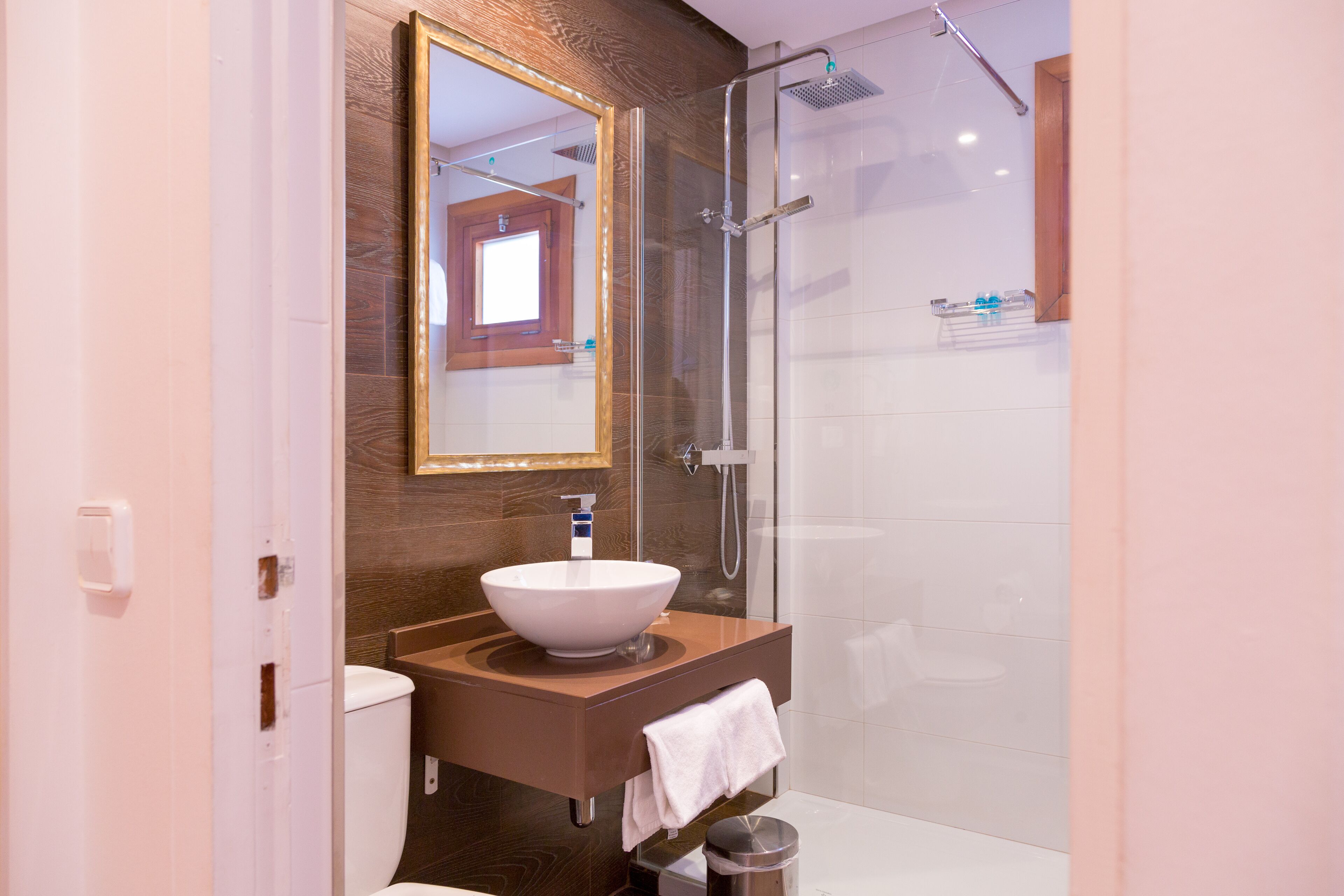 Un baño con tocador de madera, un espejo grande, un lavabo blanco y una ducha con cerramiento de vidrio.