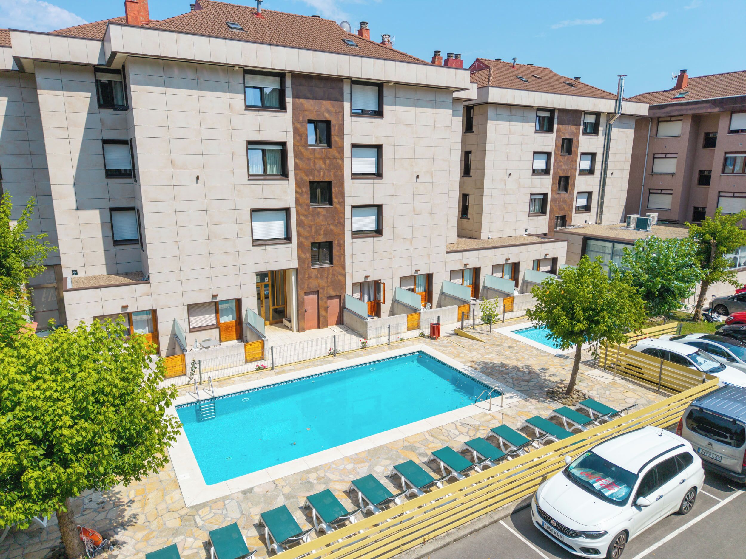 Un hotel de varios pisos con piscina, mobiliario exterior y una zona de estacionamiento.