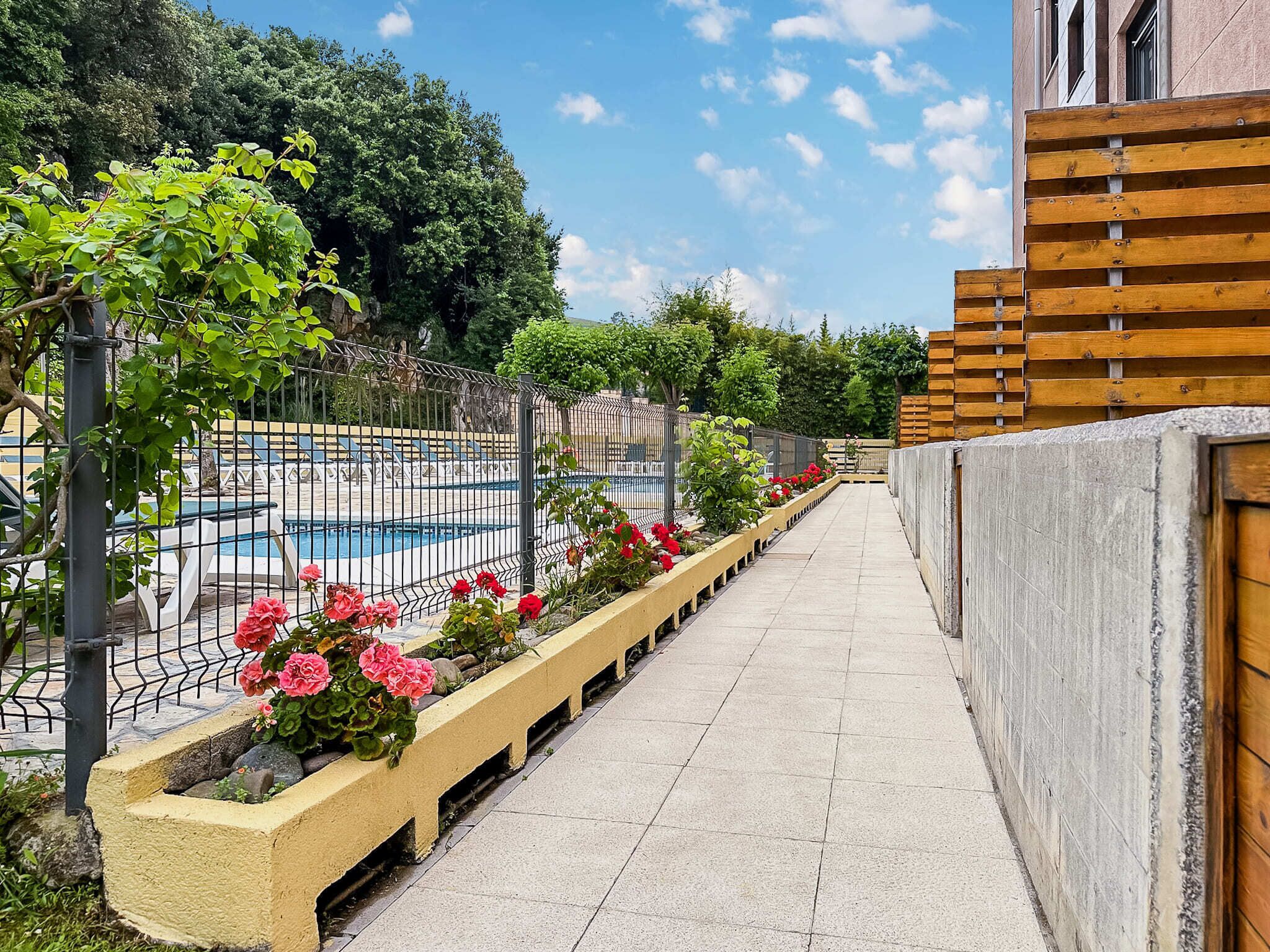 A pathway leading to a pool area with a wooden fence, flower beds, and a clear sky.