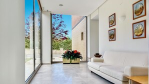 A spacious living area with a white sofa, a wooden coffee table, and a large window offering a view of the outdoors. - Hotel Los Arces (Arnuero)