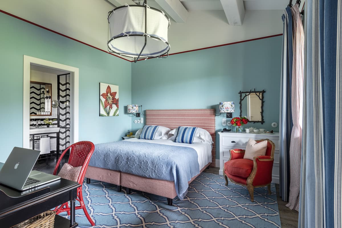 A bedroom with a bed, a desk with a laptop, a red chair, a dresser, and a mirror.