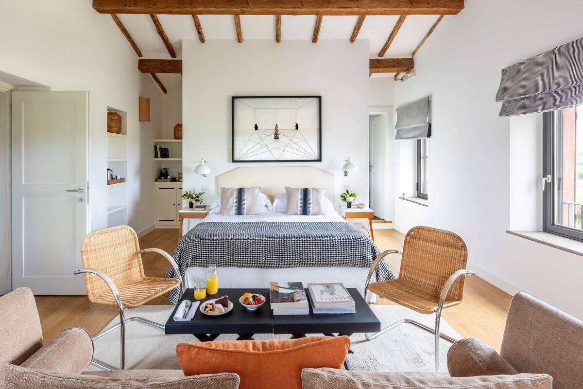 A bedroom with a bed, bedside tables, a coffee table with breakfast items, and wicker chairs.