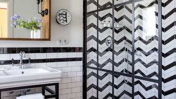 Un baño moderno con un salpicadero de azulejos a cuadros blancos y negros, un espejo grande y una zona de ducha con mampara de vidrio.