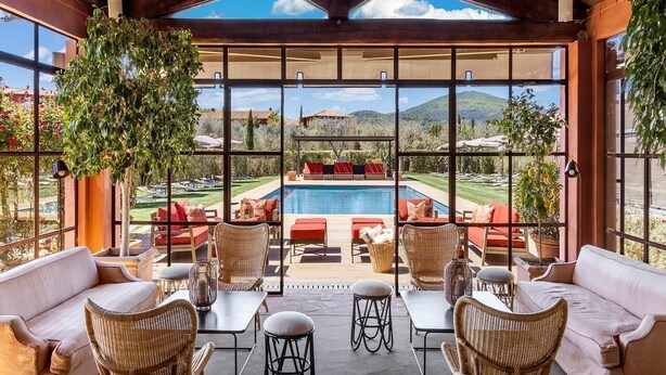 A covered outdoor seating area with wicker furniture and a view of a pool and mountains. - Resort Locanda Rossa (Capalbio)