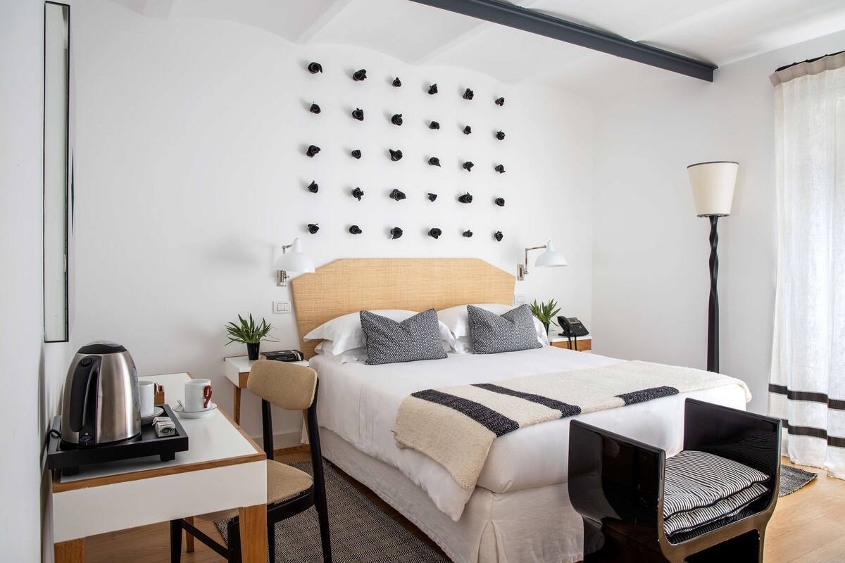 A neatly arranged hotel room with a bed, bedside tables, a desk, a chair, a wall-mounted clock, and a floor lamp.